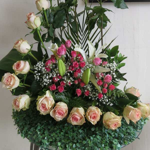Tall arrangement of cream and pink roses with white lilies and small pink roses in a curved design