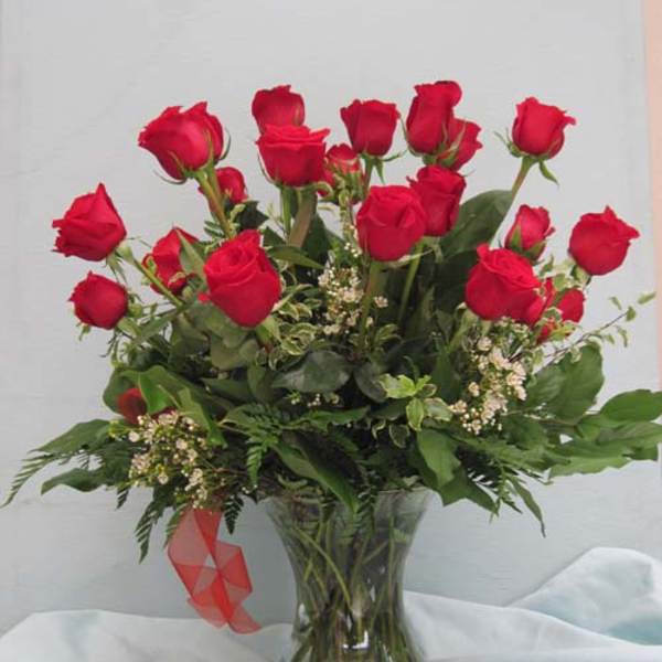 Red roses arranged in a clear glass vase with greenery