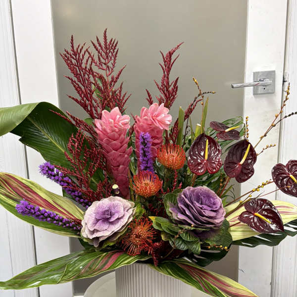 Tropical floral arrangement in a white vase with pink, purple, and burgundy blooms