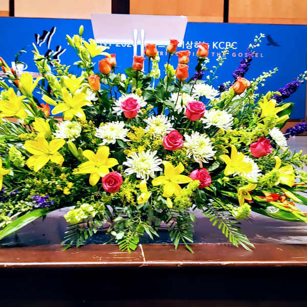 Large altar-style arrangement with yellow lilies, pink roses, and white mums on a stage