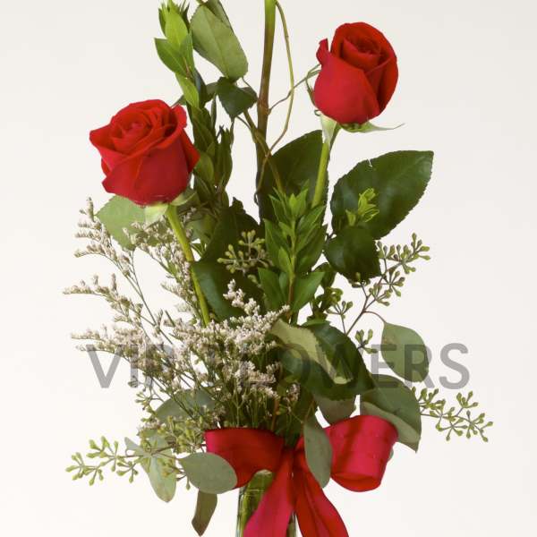 Three red roses in a tall glass vase with a red ribbon