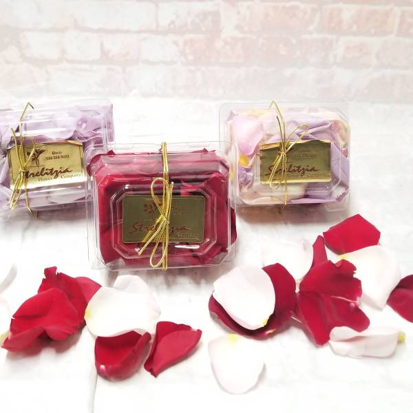 Three clear gift boxes of rose petals tied with gold ribbon.