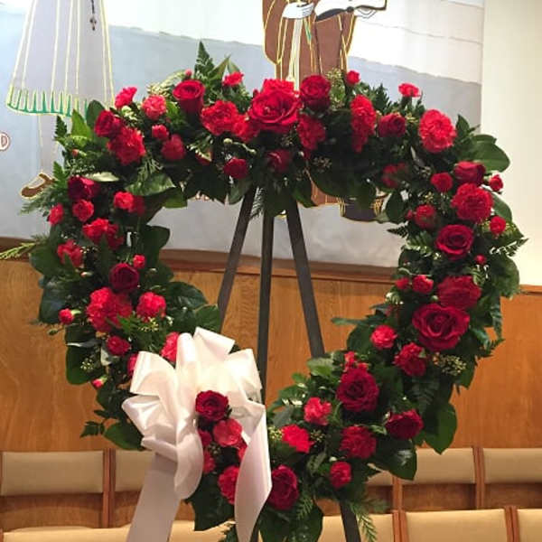 Heart-shaped red rose wreath on an easel with a white ribbon bow
