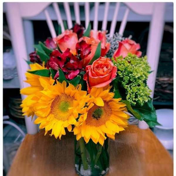 Bouquet of sunflowers, roses, and red alstroemeria in a glass vase