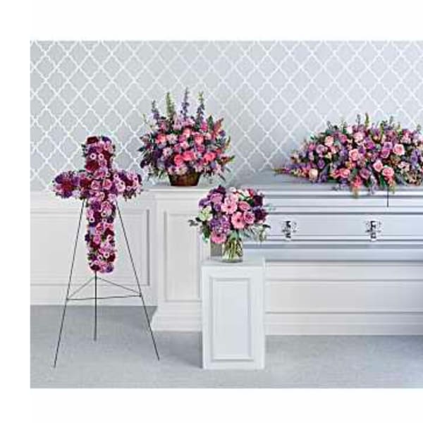 Floral funeral display with a cross, casket spray, and standing sprays in pink and purple
