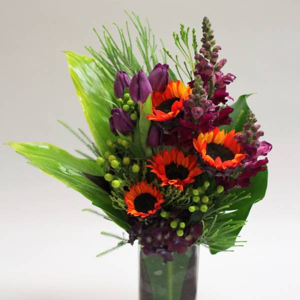 Bright bouquet of orange sunflowers and purple blooms in a clear glass vase