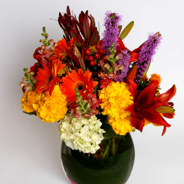 Bright mixed bouquet in a glass vase with red, orange, yellow, purple, and white blooms