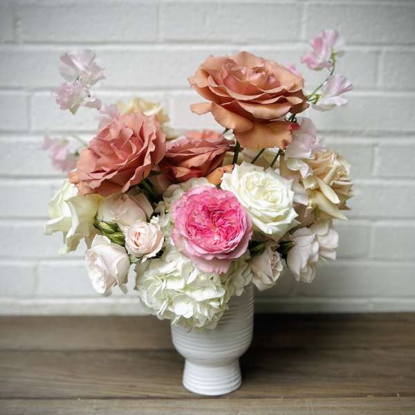 Peach, pink, and white roses arranged in a white vase
