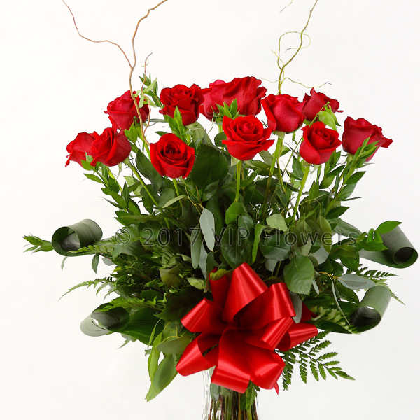 Red roses arranged in a clear glass vase with a red bow