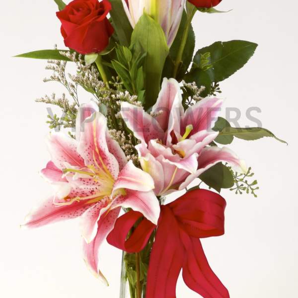 Red roses and pink lilies in a clear glass vase with a red ribbon
