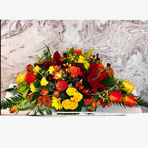 Long low arrangement of red, yellow, and orange flowers on a white base