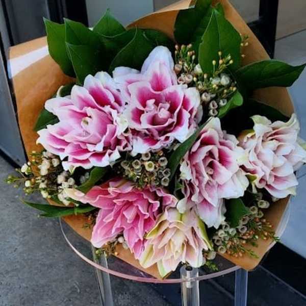 Hand-tied bouquet of pink and white blooms wrapped in brown paper