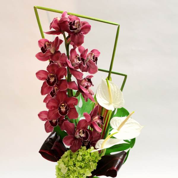 Tall orchid arrangement in a glass vase with burgundy and white blooms