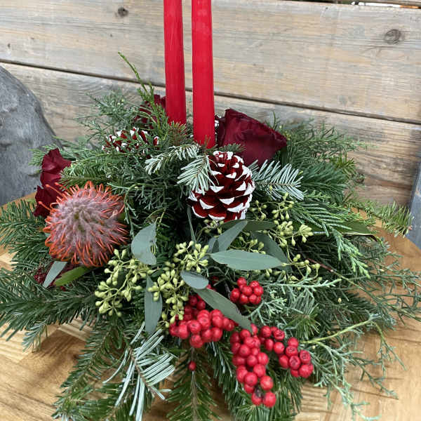 Holiday centerpiece with red candles, roses, pinecones, and evergreen branches