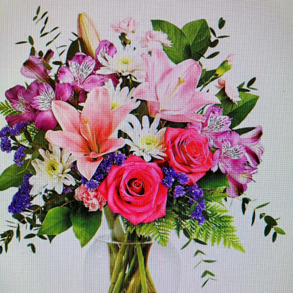Mixed bouquet of pink roses, lilies, and purple flowers in a glass vase