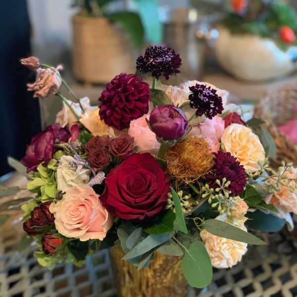 Mixed bouquet of roses and dark blooms in a gold vase