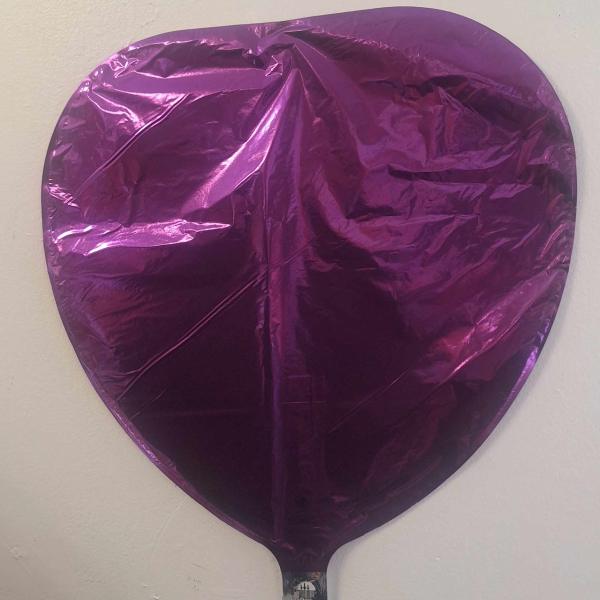 Purple heart-shaped foil balloon against a plain wall