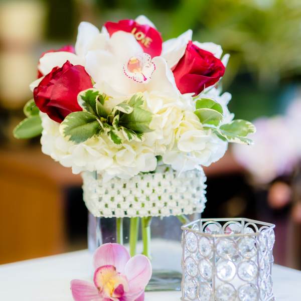 White hydrangea and red roses in a clear vase with a pink orchid bloom