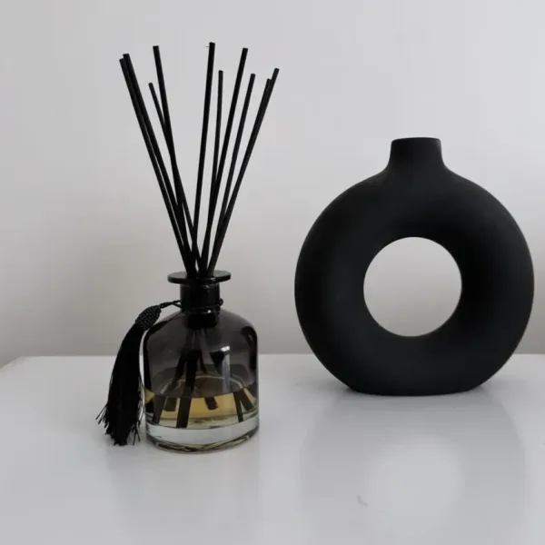 Black reed diffuser bottle with a round black vase beside it