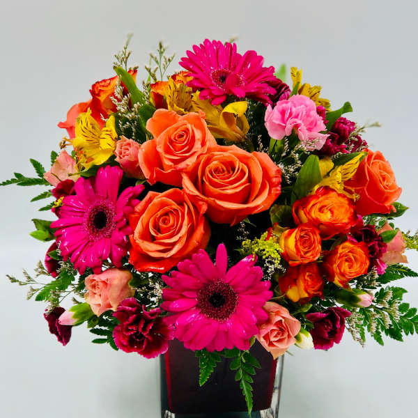 Bright mixed bouquet of roses, gerbera daisies, and carnations in a square vase