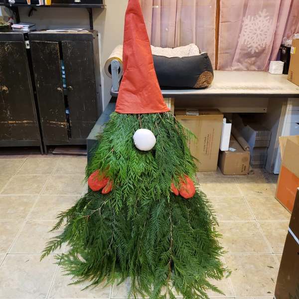 A gnome-shaped decoration made of greenery with a red hat and white nose