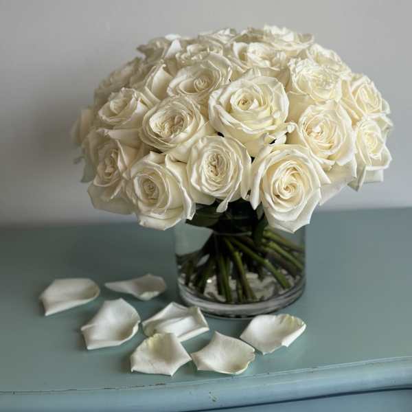 Bouquet of white roses in a clear glass vase with scattered petals