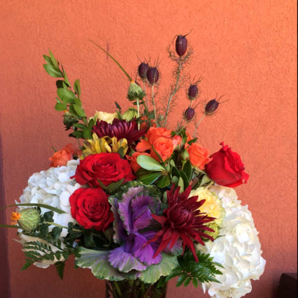 Mixed bouquet of roses, hydrangeas, and purple blooms in a glass vase