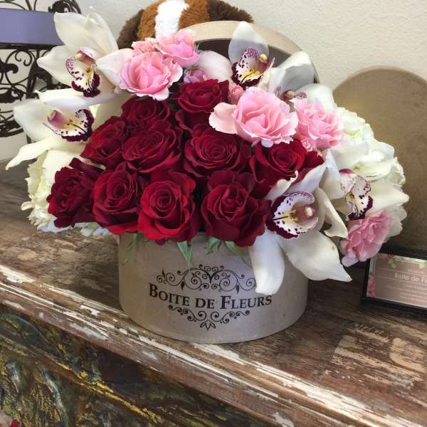 Bouquet of red and pink roses with white orchids in a round box
