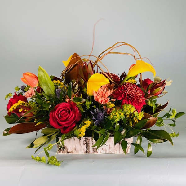 Mixed floral arrangement in a rustic rectangular container with red, yellow, and orange blooms