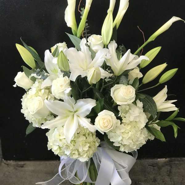 White lilies and roses arranged in a glass vase with a white ribbon