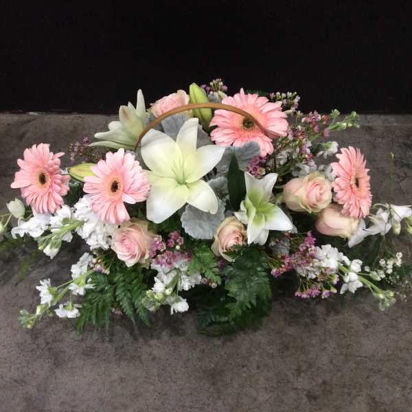 Pink gerbera daisies and white lilies arranged with roses in a low basket.