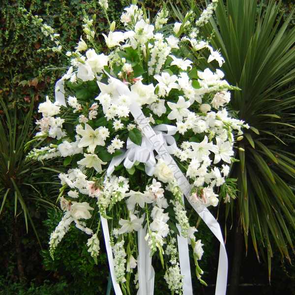Large white funeral spray on a stand with ribbon streamers