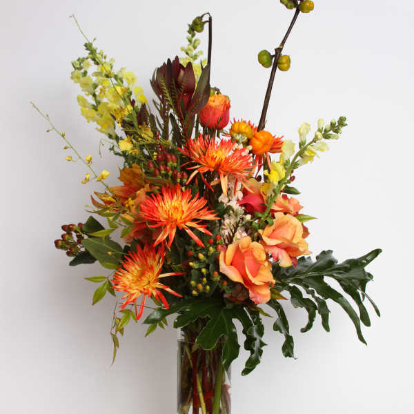 Tall mixed bouquet in a clear glass vase with orange and yellow blooms