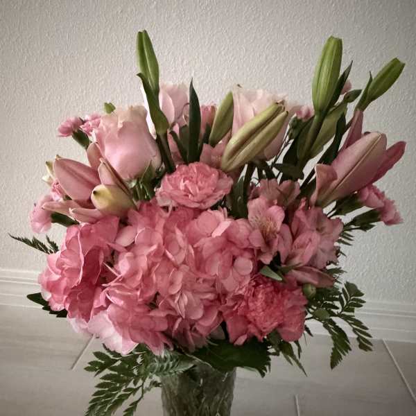 Pink bouquet with hydrangeas, lilies, and carnations in a clear glass vase