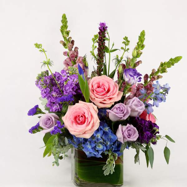 Mixed bouquet of pink, purple, and blue flowers in a glass vase
