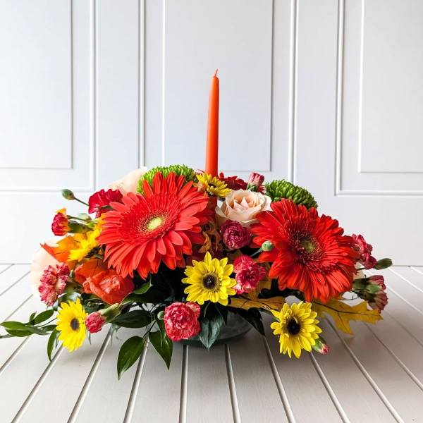 Low floral centerpiece with red gerberas and a tall orange candle