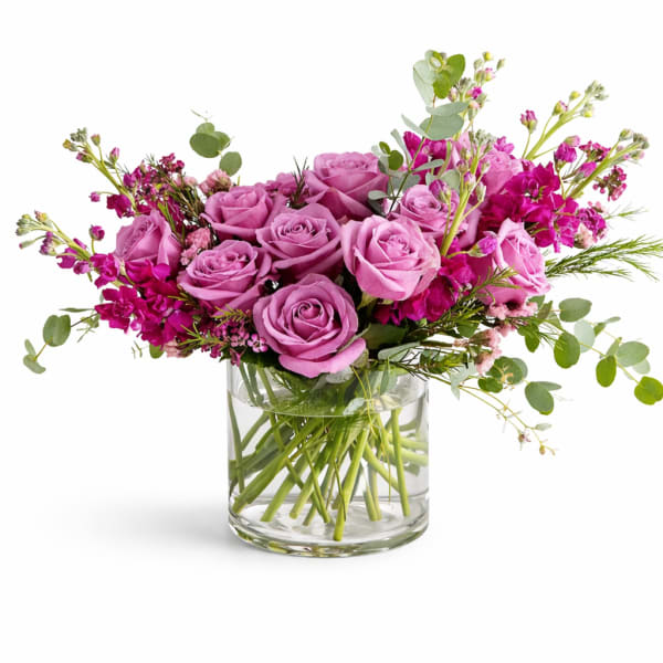 Pink roses and magenta flowers arranged in a clear glass vase