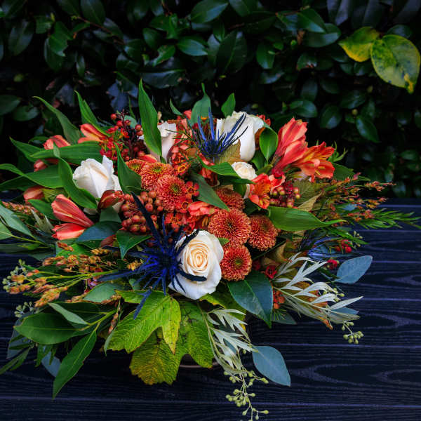 Low floral arrangement with orange, white, and blue blooms on a dark table