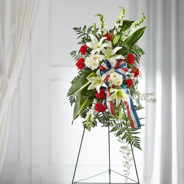 Standing floral spray with white lilies, red carnations, and ribbon on an easel