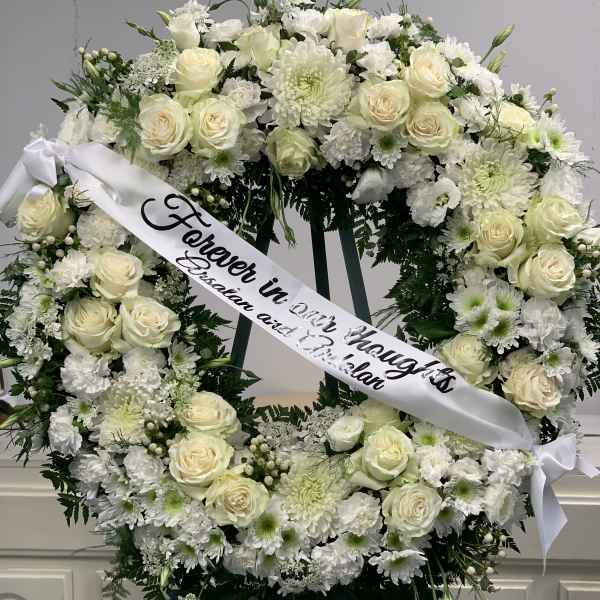 White floral funeral wreath with a memorial ribbon on an easel