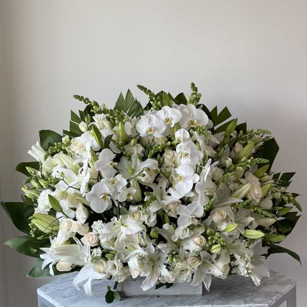 Large white floral arrangement with orchids and lilies in a low container