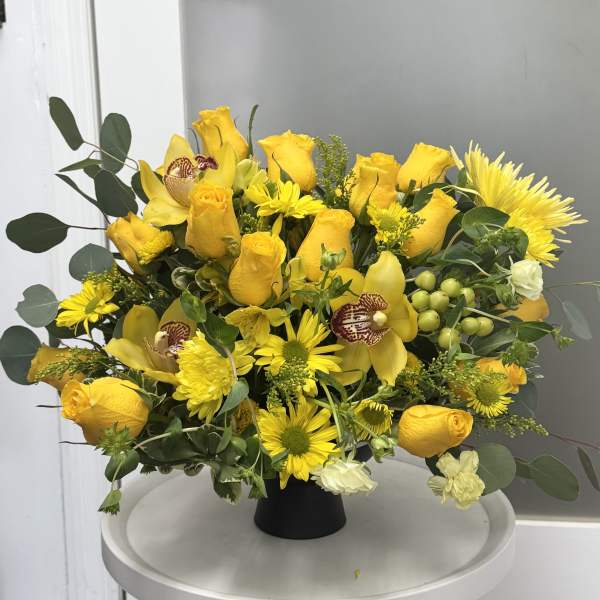 Yellow roses and daisies arranged in a black vase with green foliage.