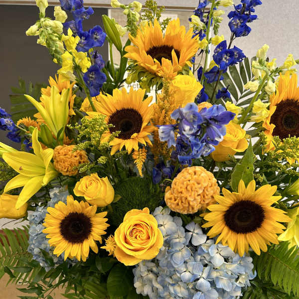 Bright bouquet of sunflowers, yellow roses, blue hydrangeas, and lilies in a white vase