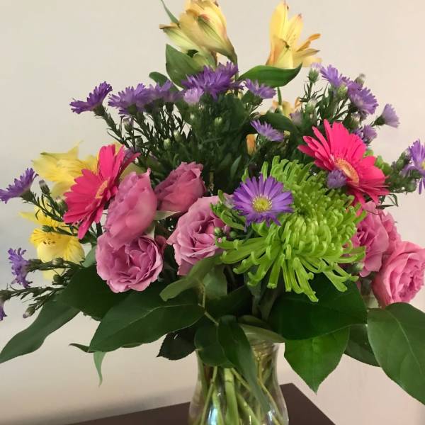 Mixed bouquet of pink roses, gerbera daisies, and purple flowers in a glass vase