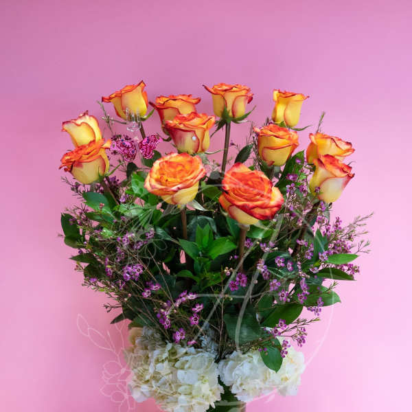 Orange-yellow roses in a tall vase with white hydrangeas and purple filler flowers