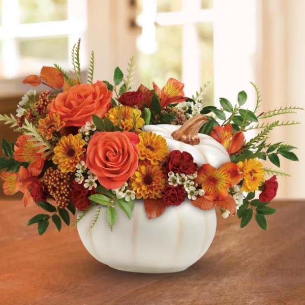 Orange and red floral arrangement in a white pumpkin vase