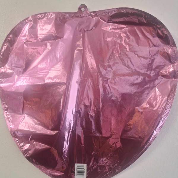 Pink metallic heart-shaped balloon against a plain wall