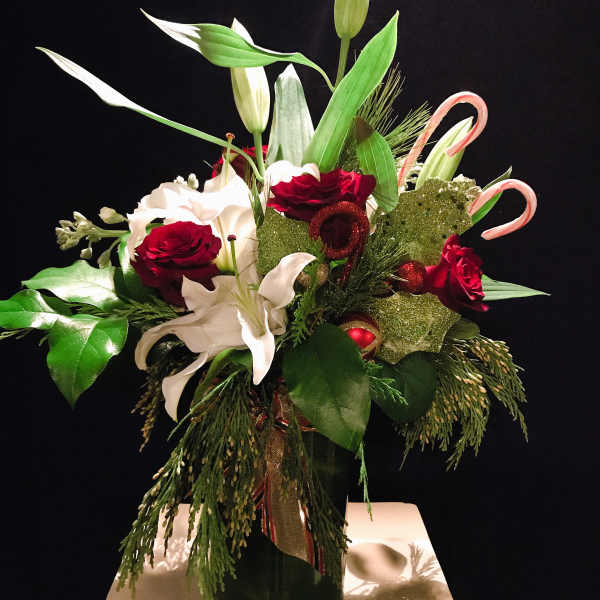 Holiday bouquet with red roses, white lilies, and candy cane accents in a vase