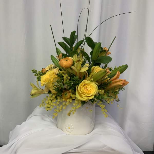 Yellow roses and lilies arranged in a white ceramic pot