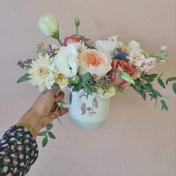 Handheld bouquet of pastel roses and white blooms in a white mug vase